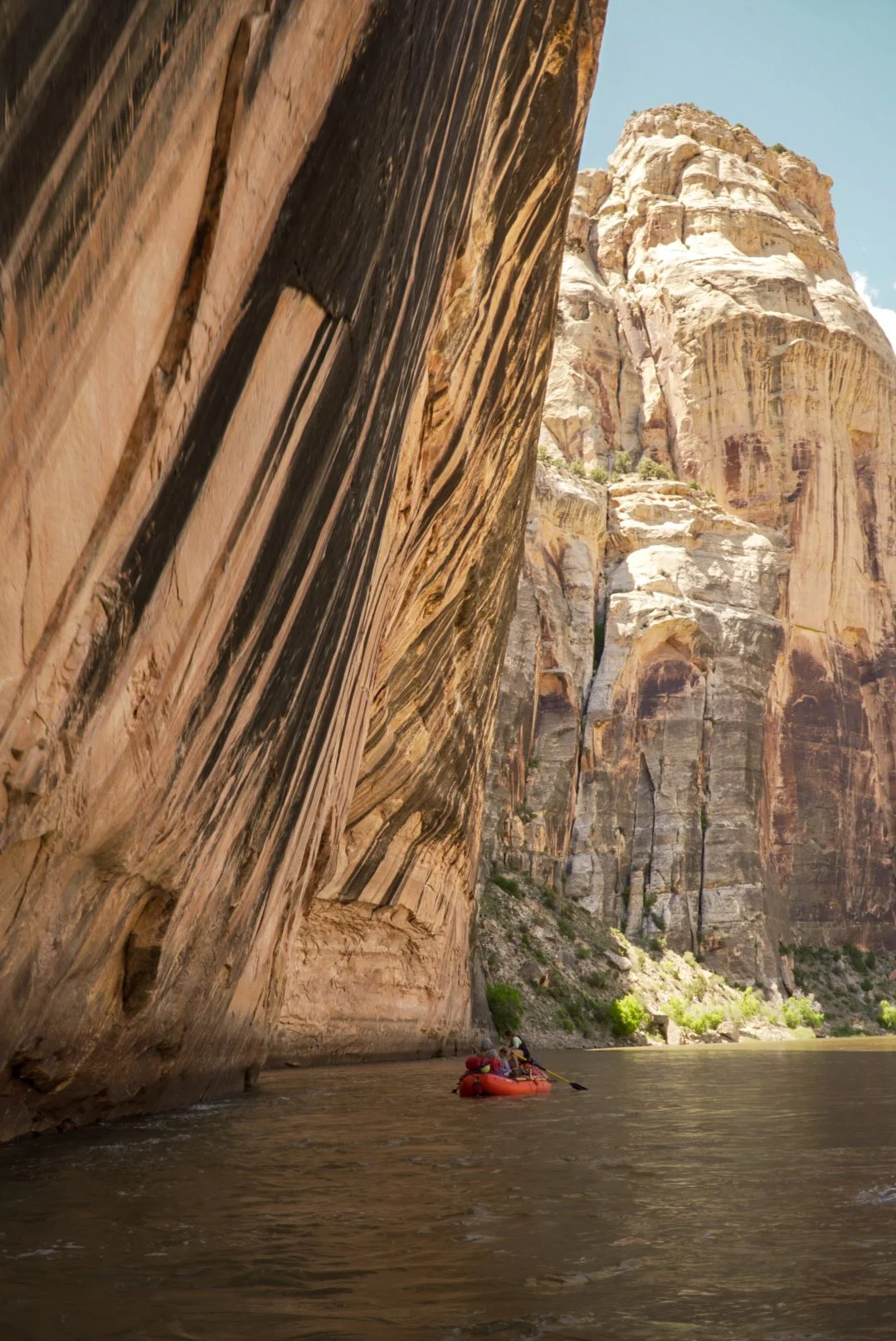 A person kayaking on a river with steep, colorful canyon walls towering above.