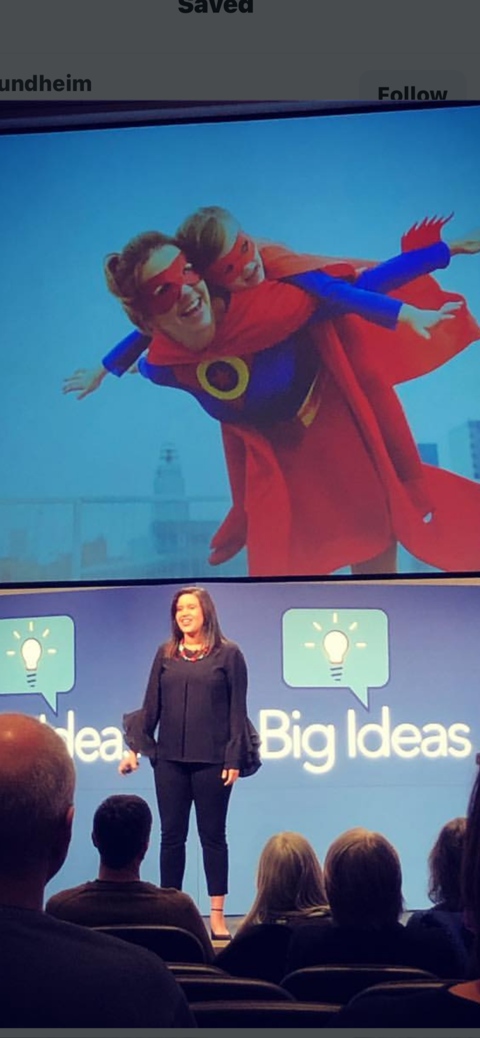 A woman in a black outfit giving a presentation on stage with a blue background displaying the logo "Big Ideas".