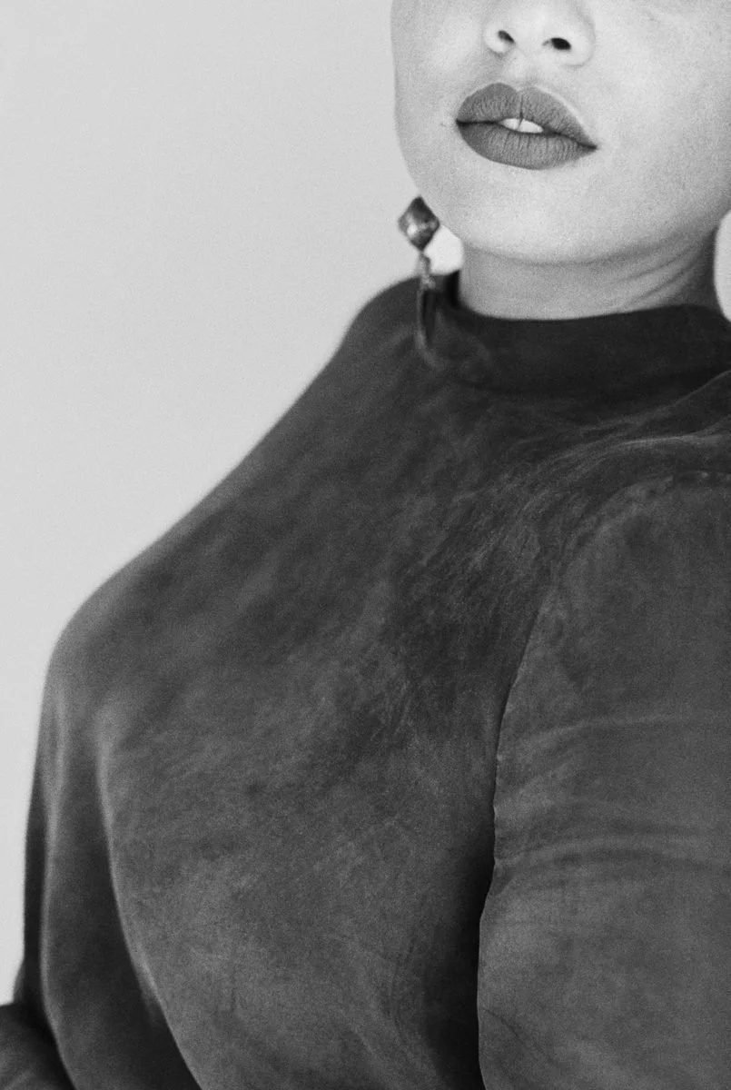 Close-up of a woman with dark lipstick and earrings, wearing a dark top.