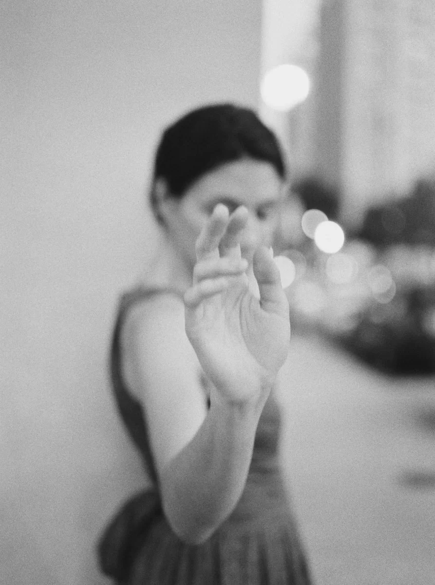 A woman in a sleeveless top reaching out towards the camera with her hand, blurred background with bokeh lights
