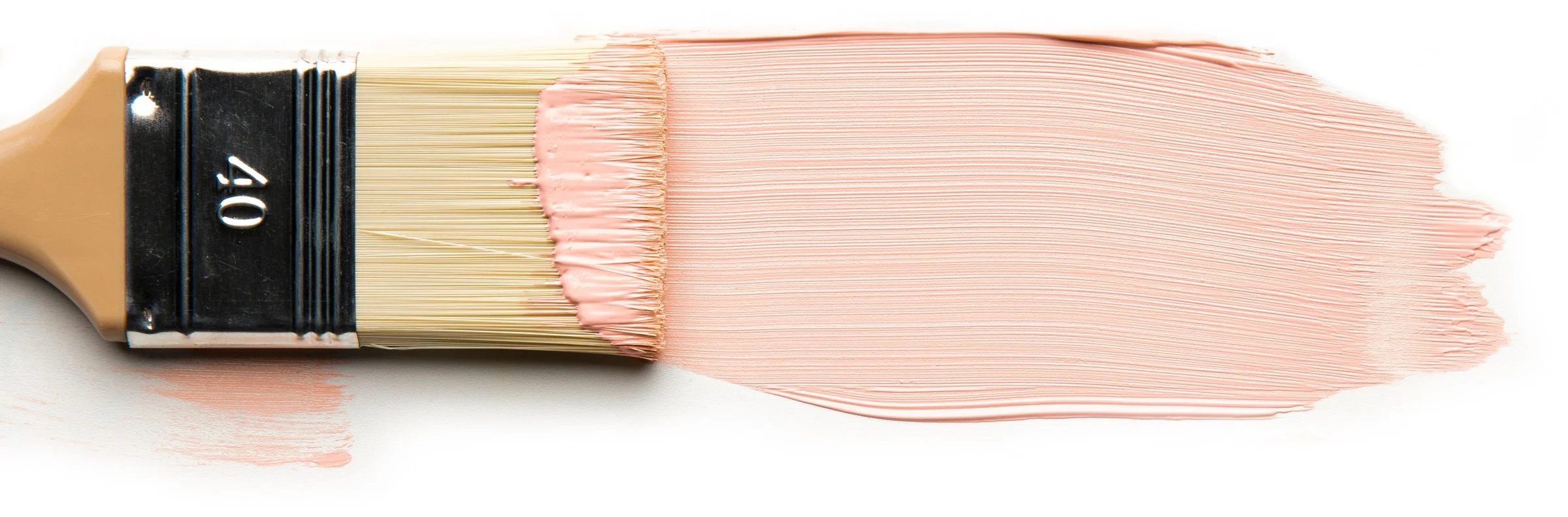 Paintbrush applying light pink paint on a white surface close-up.