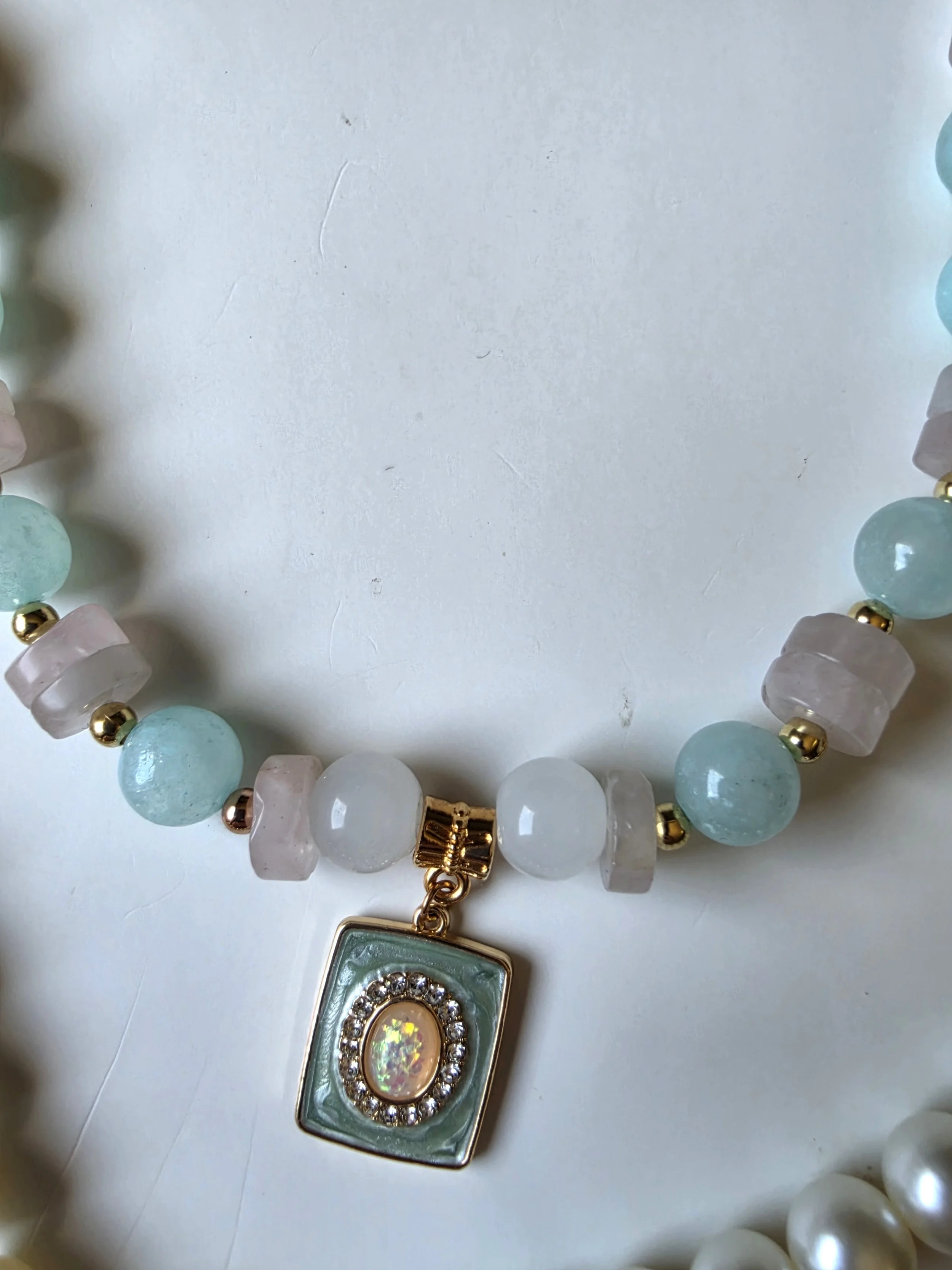 Part of a necklace with pink, blue and gold beads.  There is a blue and pink charm in the centre.