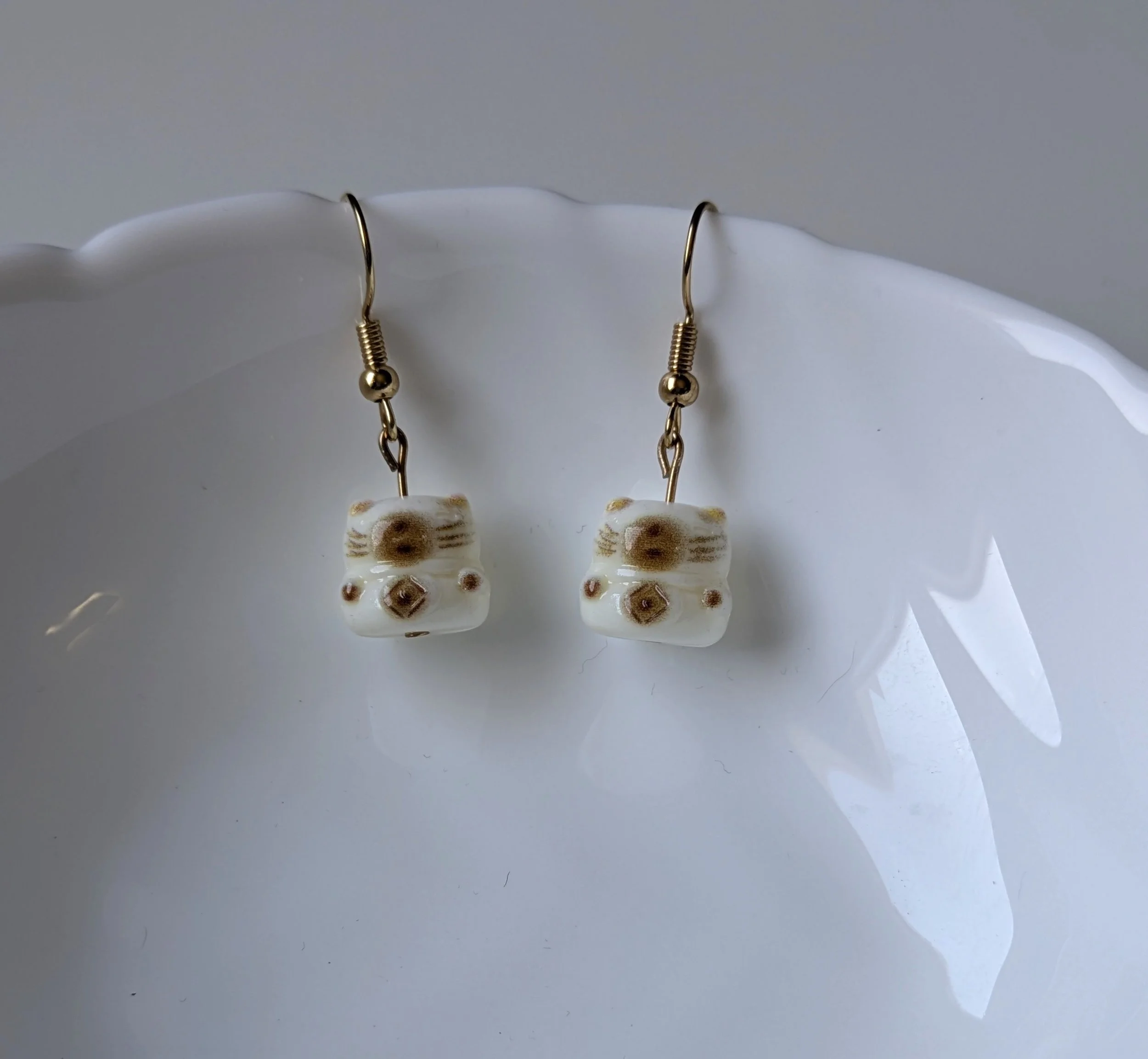 A pair of gold earrings with a small white and brown kitten charm.