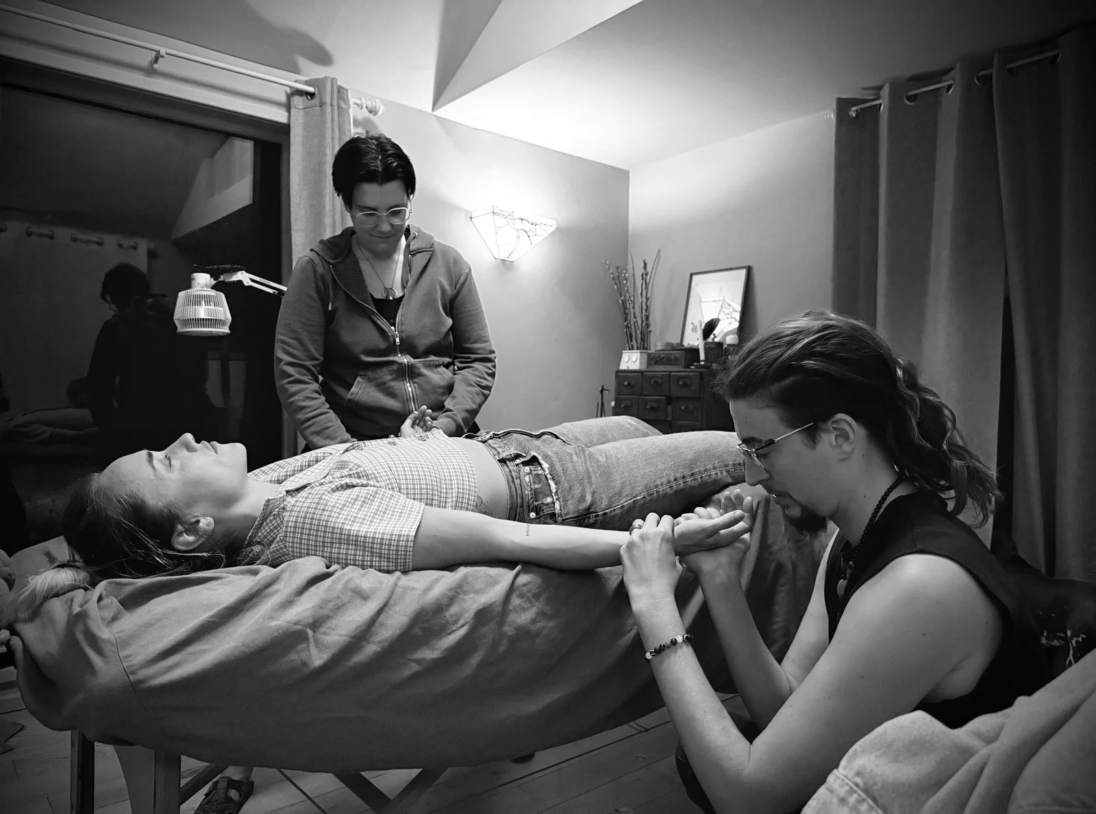 A person lying face-up on a massage bed while receiving 4-hands treatment from both Kyng & Edea at the same time. On their legs Mu, a small dog, provides additional support.
