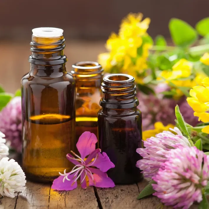 Three amber glass essential oil bottles surrounded by pink, white, and yellow flowers on a wooden surface.