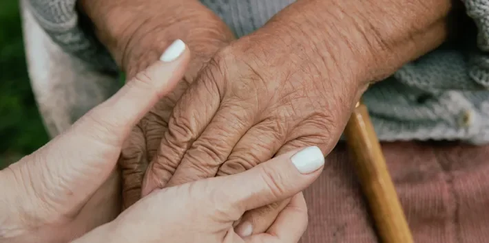 Close-up of two hands gently holding each other, one appearing older and the other younger.