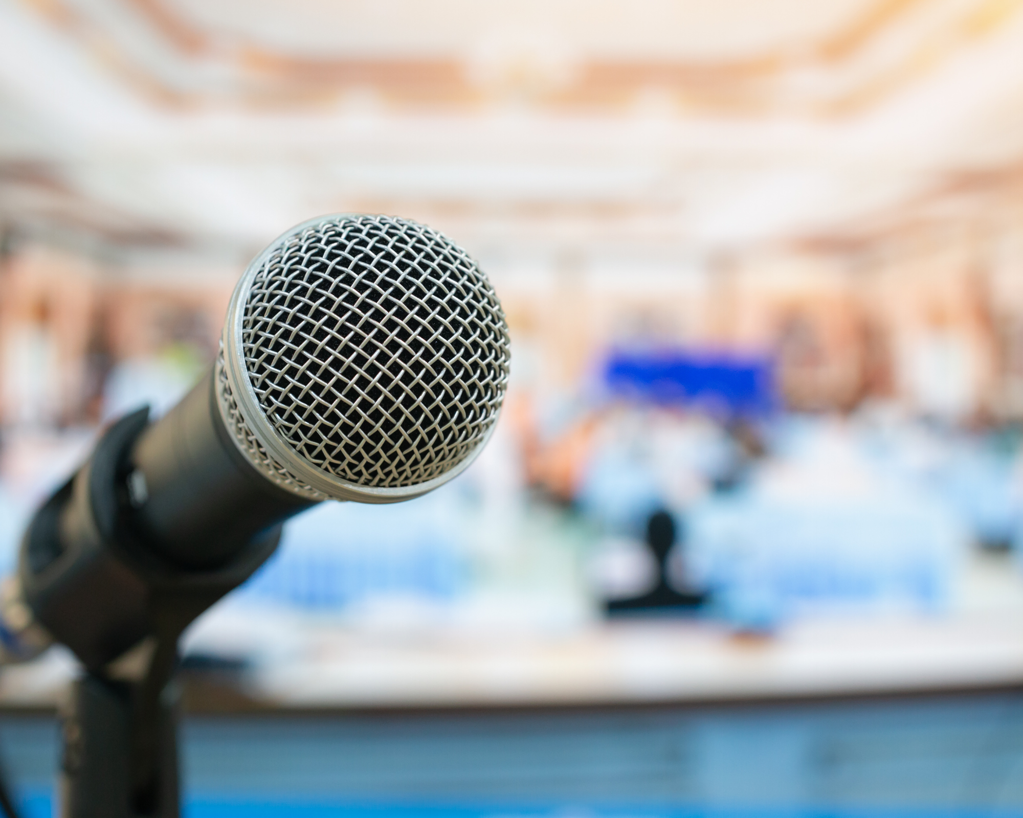 Close-up of a microphone on a stand in front of a blurred background of bookshelves.