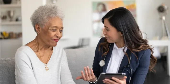 A young female healthcare professional consulting with an elderly woman in a therapy or counseling session.