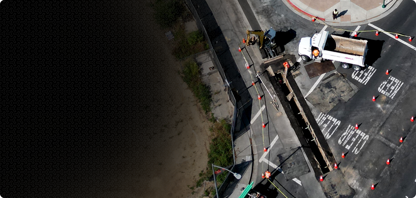 Bird's eye view of a road construction site with a utility truck and construction equipment, surrounded by orange traffic cones, with work crews present.