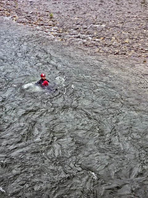 Swift Water Rescue Training - A person in a red life jacket and helmet swimming in a river.