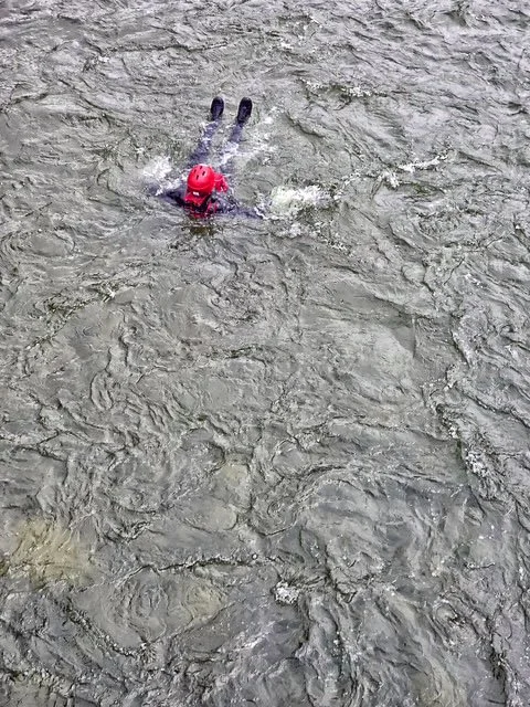 Swift Water Rescue Training - Person wearing a pink helmet and black wetsuit swimming in a muddy river.