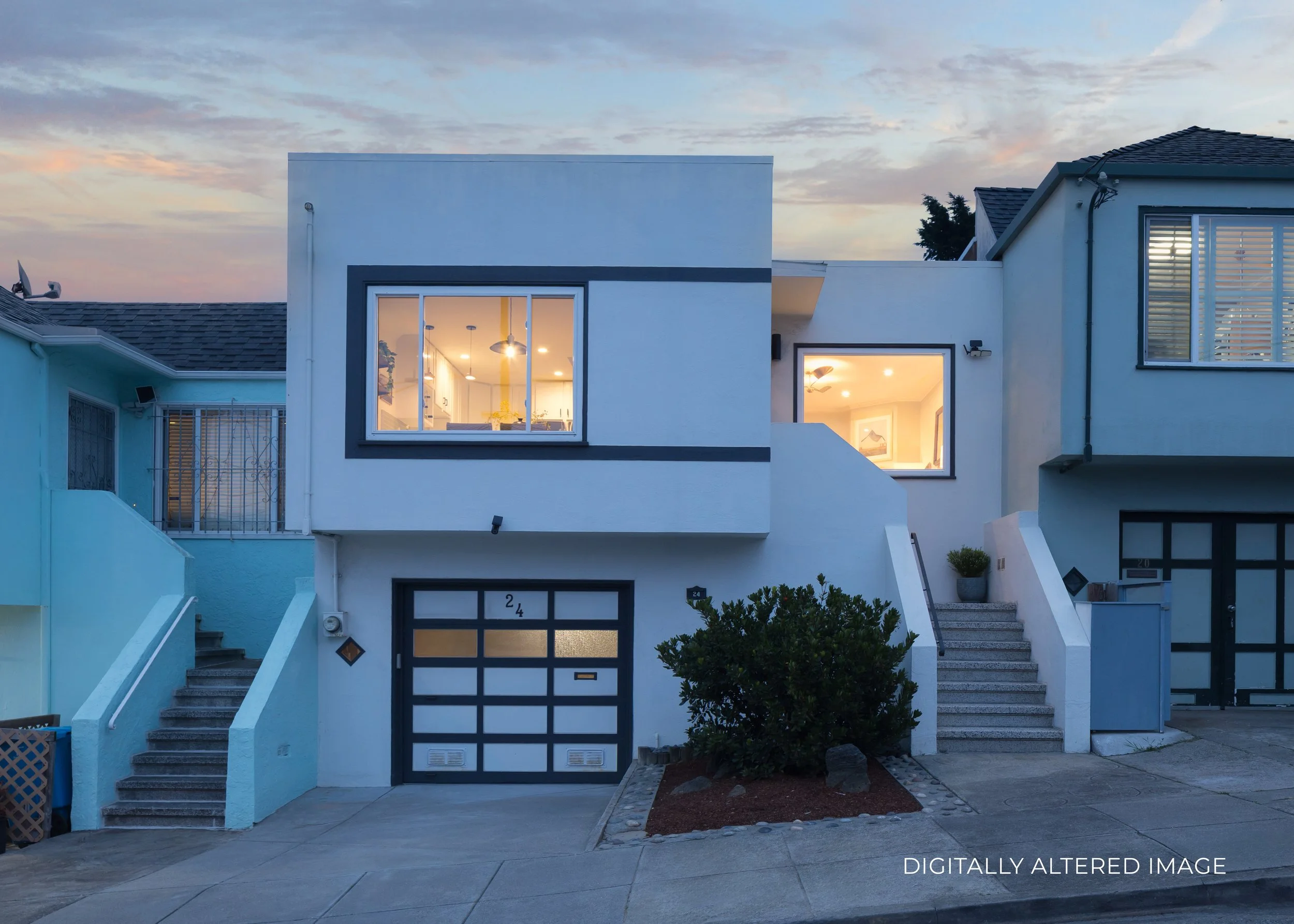 Modern two-story house with white and dark gray accents, large windows lit from inside, staircase with stairs leading up to the front door, small landscaping with bushes and rocks in front, neighboring houses, and a sunset sky in the background.
