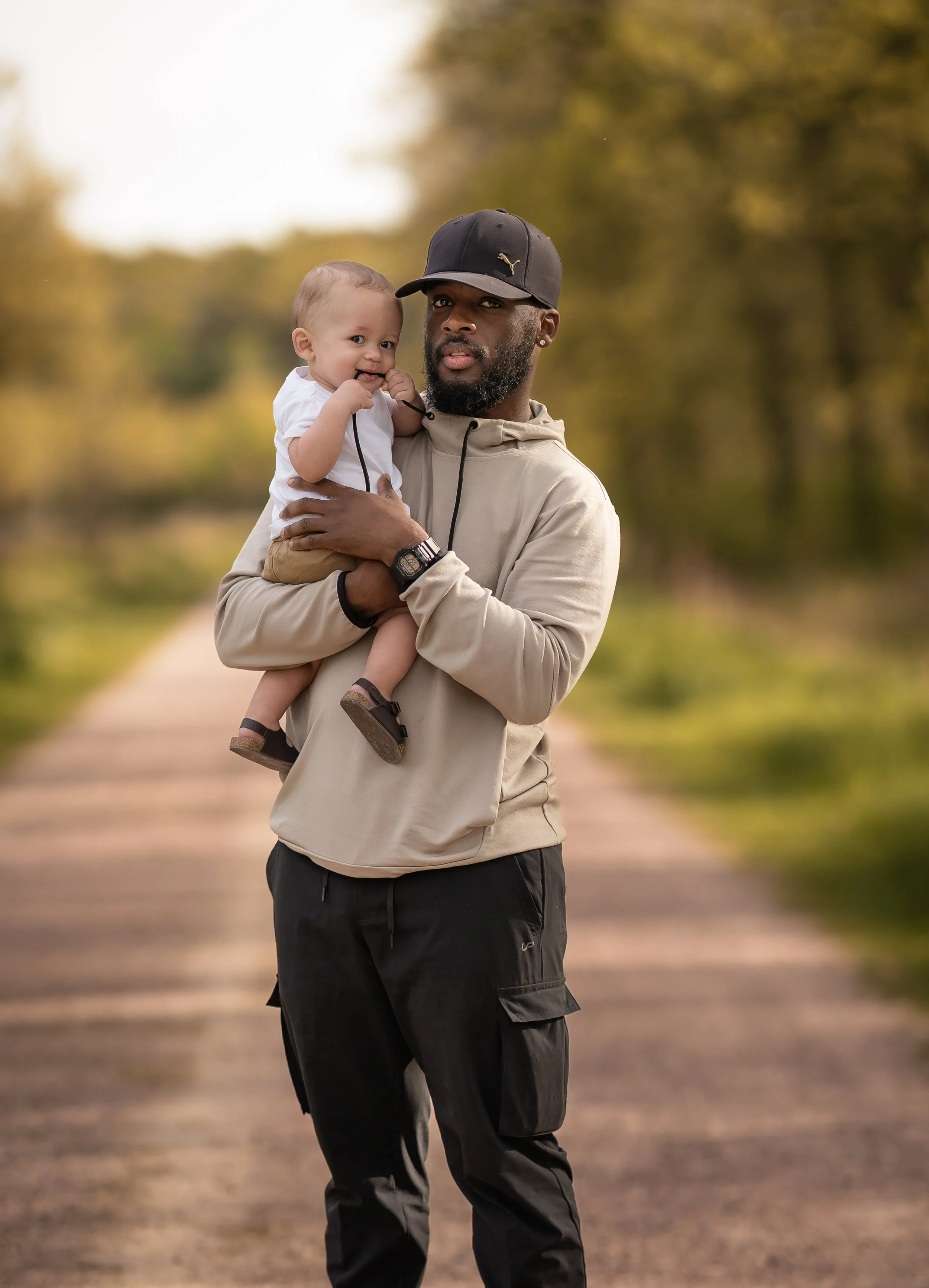 A man holding a smiling child while walking on a tree-lined path outdoors during daytime.