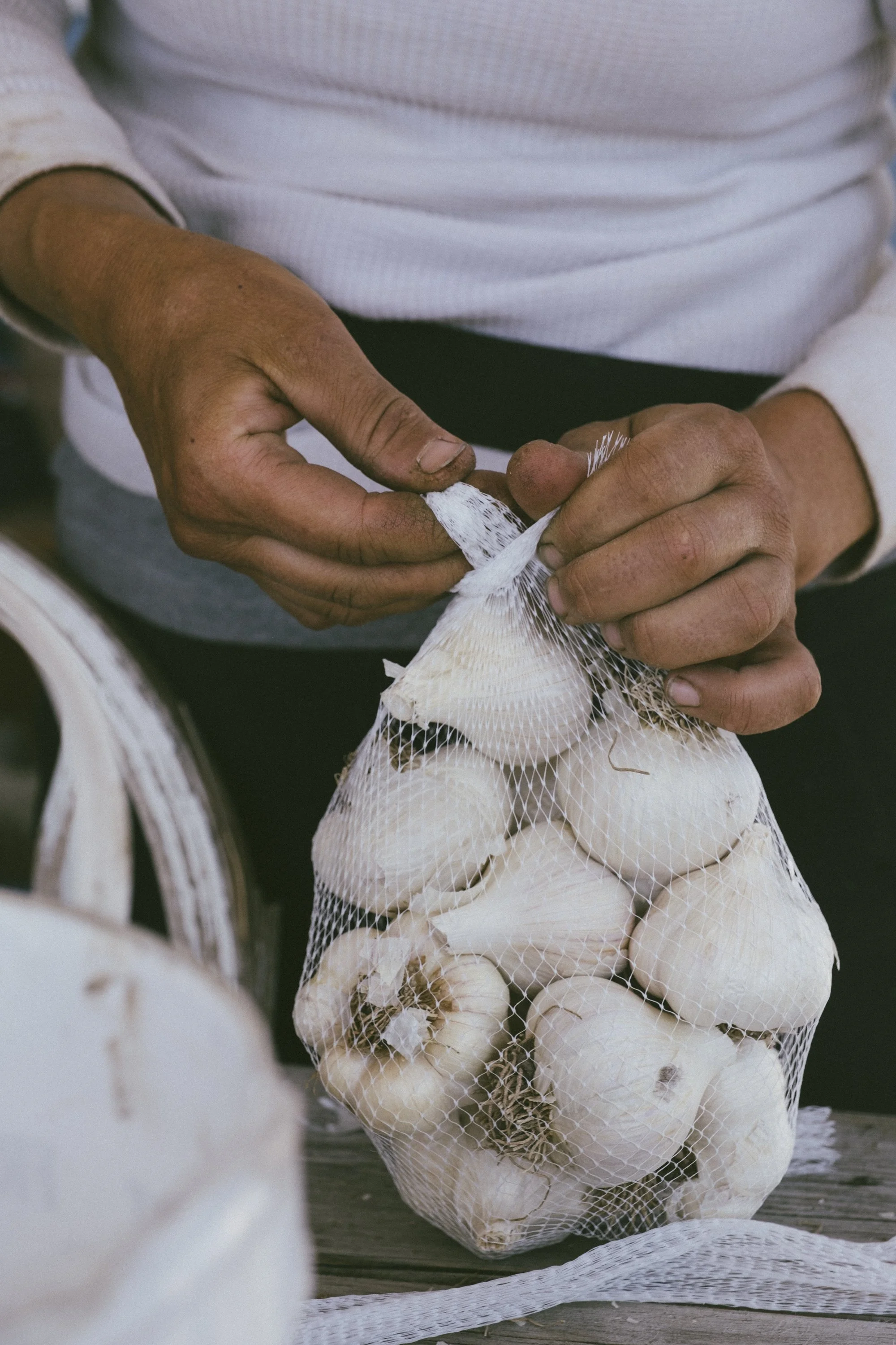 A person tying a mesh bag full of white garlic