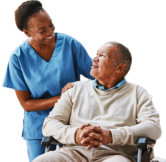 A female healthcare worker in blue scrubs smiling at an elderly man sitting in a wheelchair, who is smiling back.