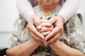 A caregiver gently holding an elderly woman's hands.