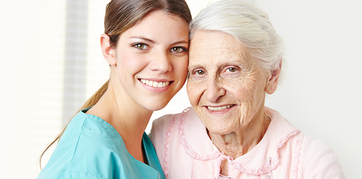 Personal Care - Home Care - Specialized Care - Disability Care - Post Hospital Care - Memory care - Dementia care - Companion  Care - 24/7 Care - A Rosebuds' caregiver smiling with an elderly woman in a care setting.