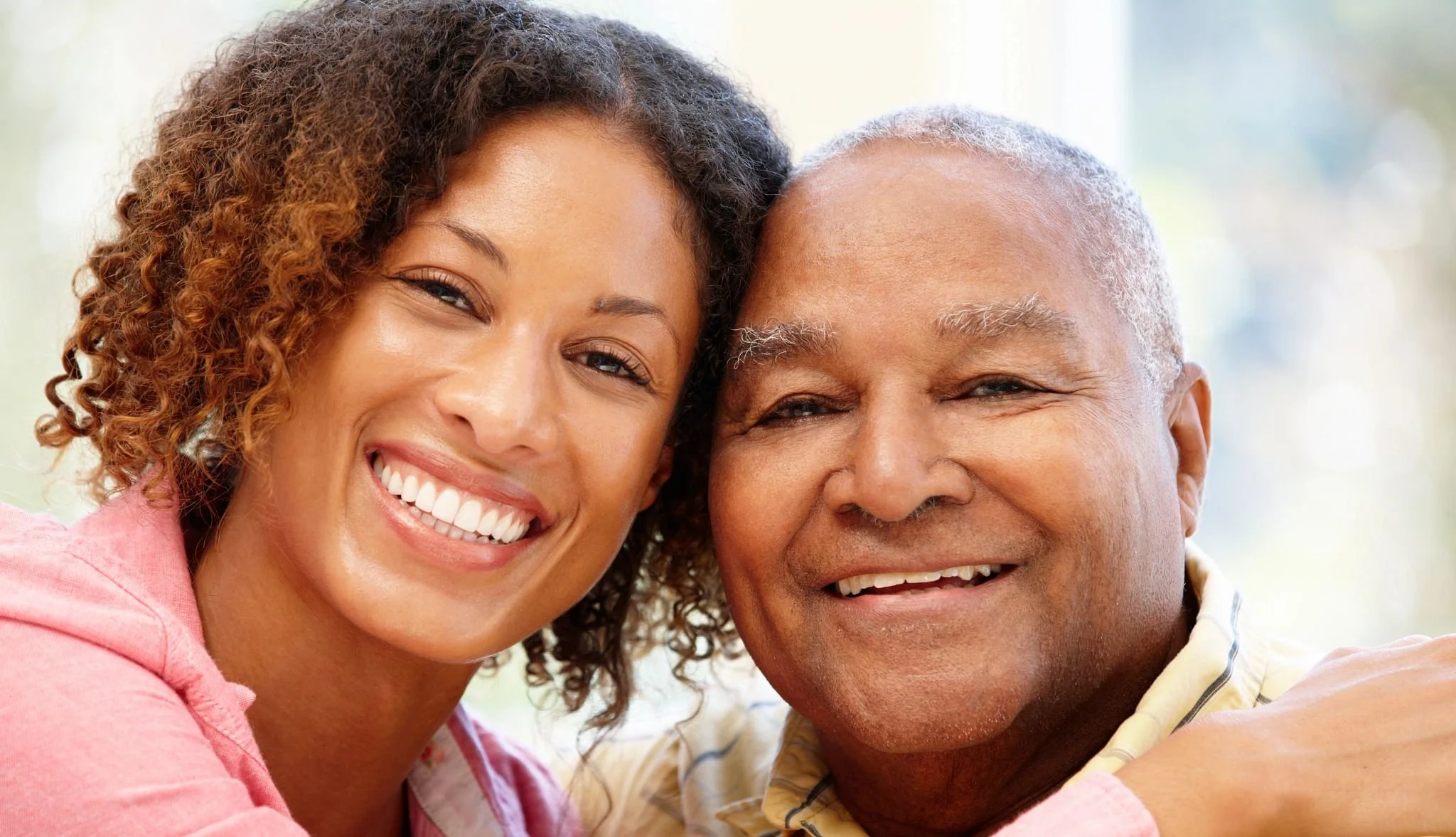 Personal Care - Home Care - Specialized Care - Disability Care - Post Hospital Care - Memory care - Companion care -  A smiling young Rosebuds' caregiver with curly hair and an older man with short gray hair, both happy and close together.