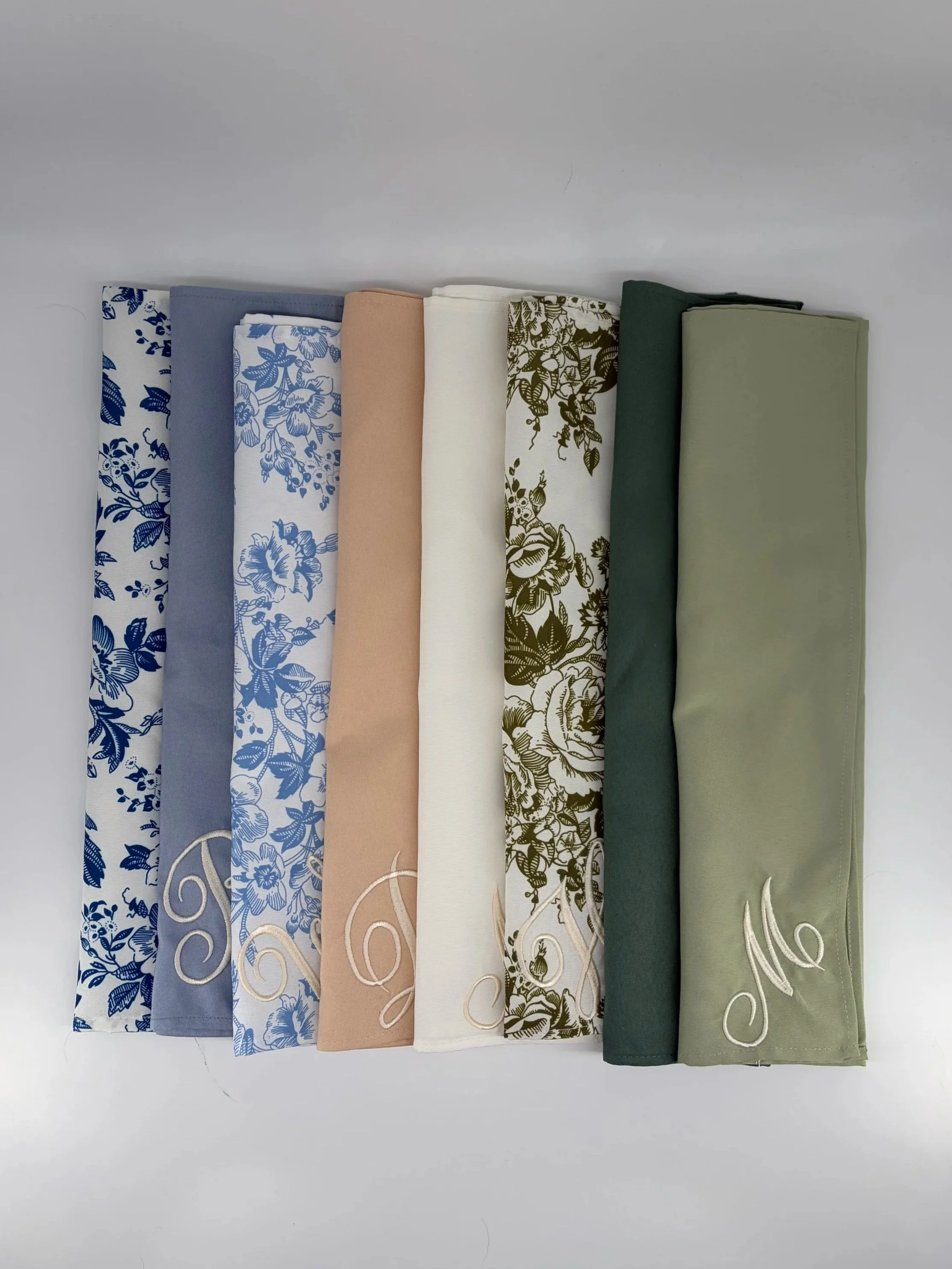 Six folded fabric pieces arranged in a row with various colors and patterns, including floral designs, plain, and embroidered sections.