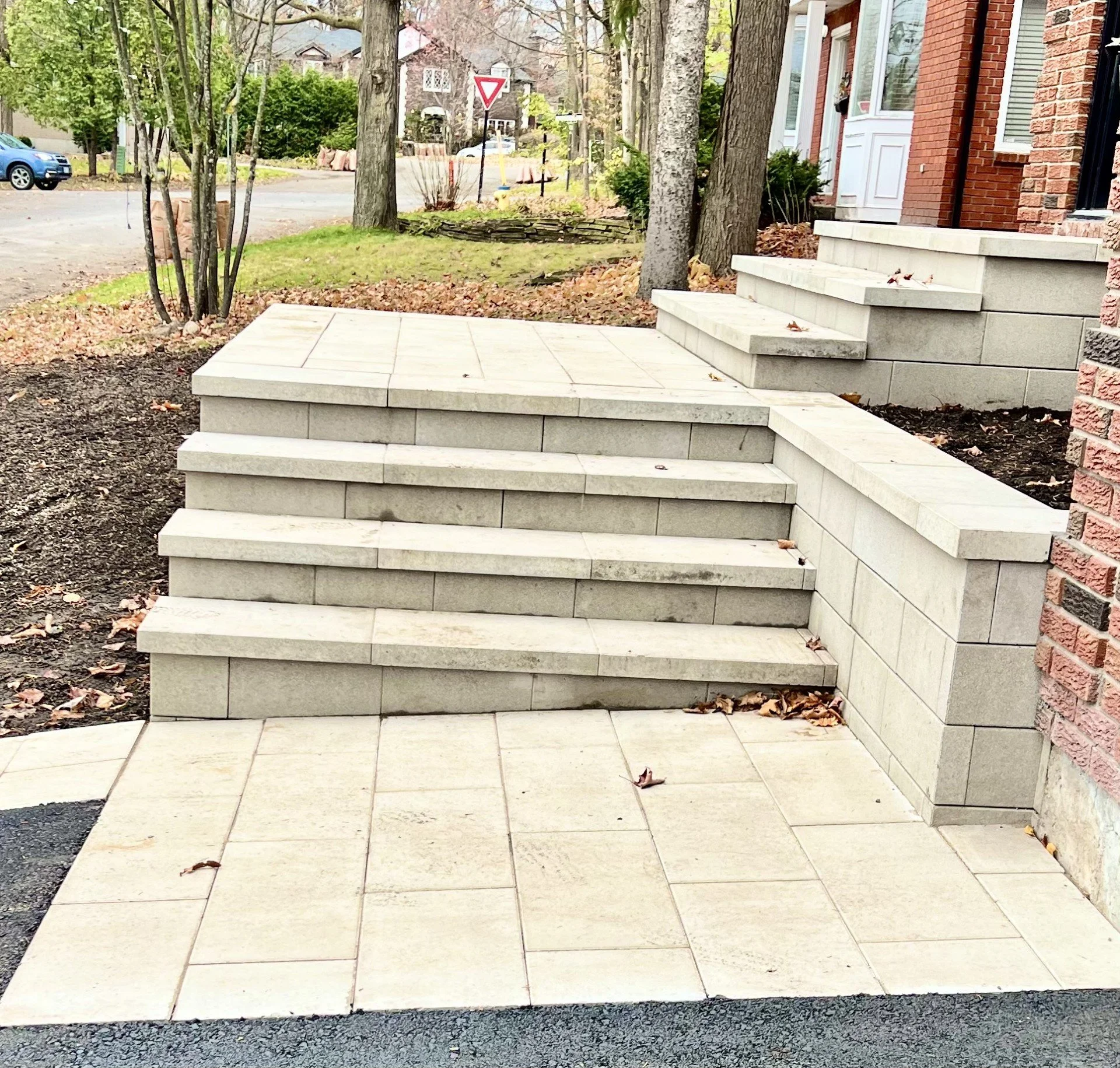 Newly constructed stone front steps and landing leading to a house entrance, with a brick wall on the right, in a suburban neighborhood with trees and houses in the background.