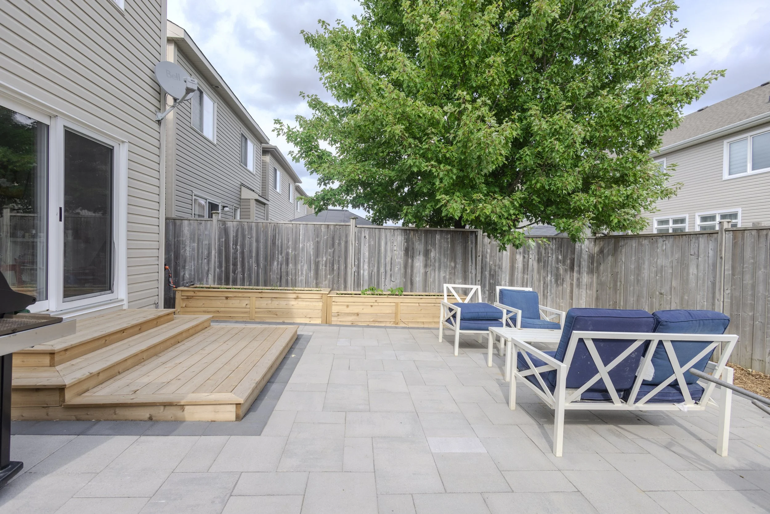 Backyard patio with interlock pavers, wood deck, and seating area in Ottawa