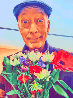 Person wearing a cap holding a colorful bouquet of flowers, with a clear sky background.