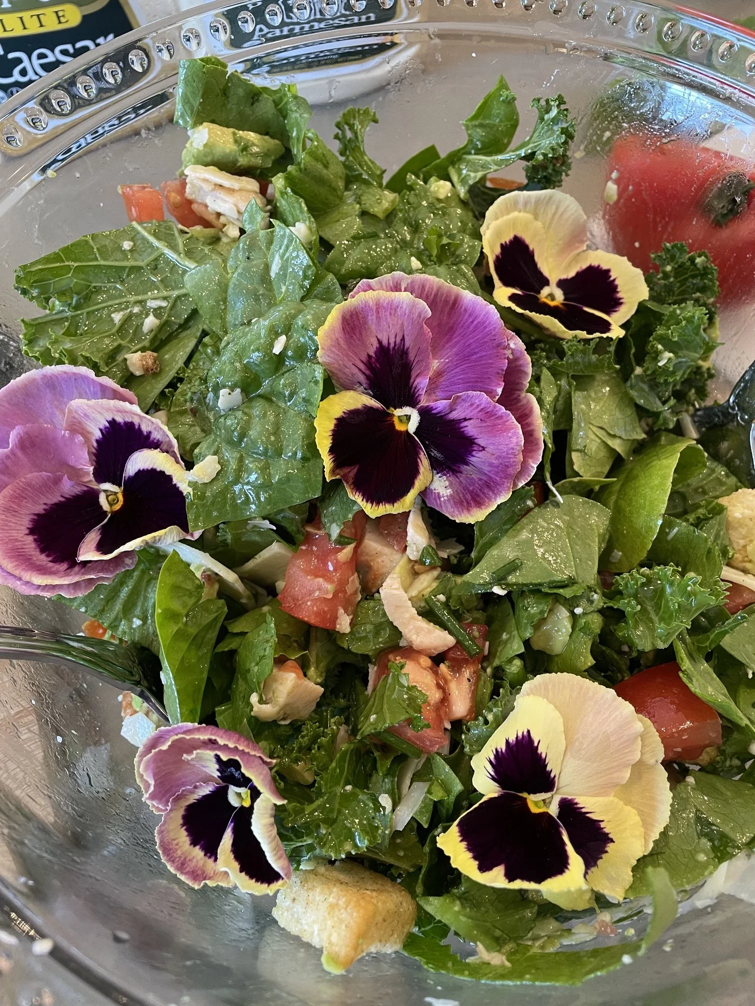 Close-up of a bowl of fresh mixed salad with lettuce, cherry tomatoes, and edible flowers, with some crushed nuts or cheese sprinkled on top.