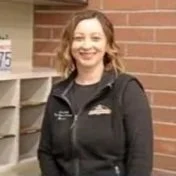 Woman with curly red hair smiling, standing outside near mailbox with brick wall in background.
