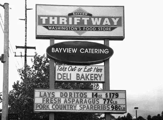 A sign for Thrift Way food store and Bayview Catering with menu prices for Lay's Doritos, fresh asparagus, and pork country spareribs.