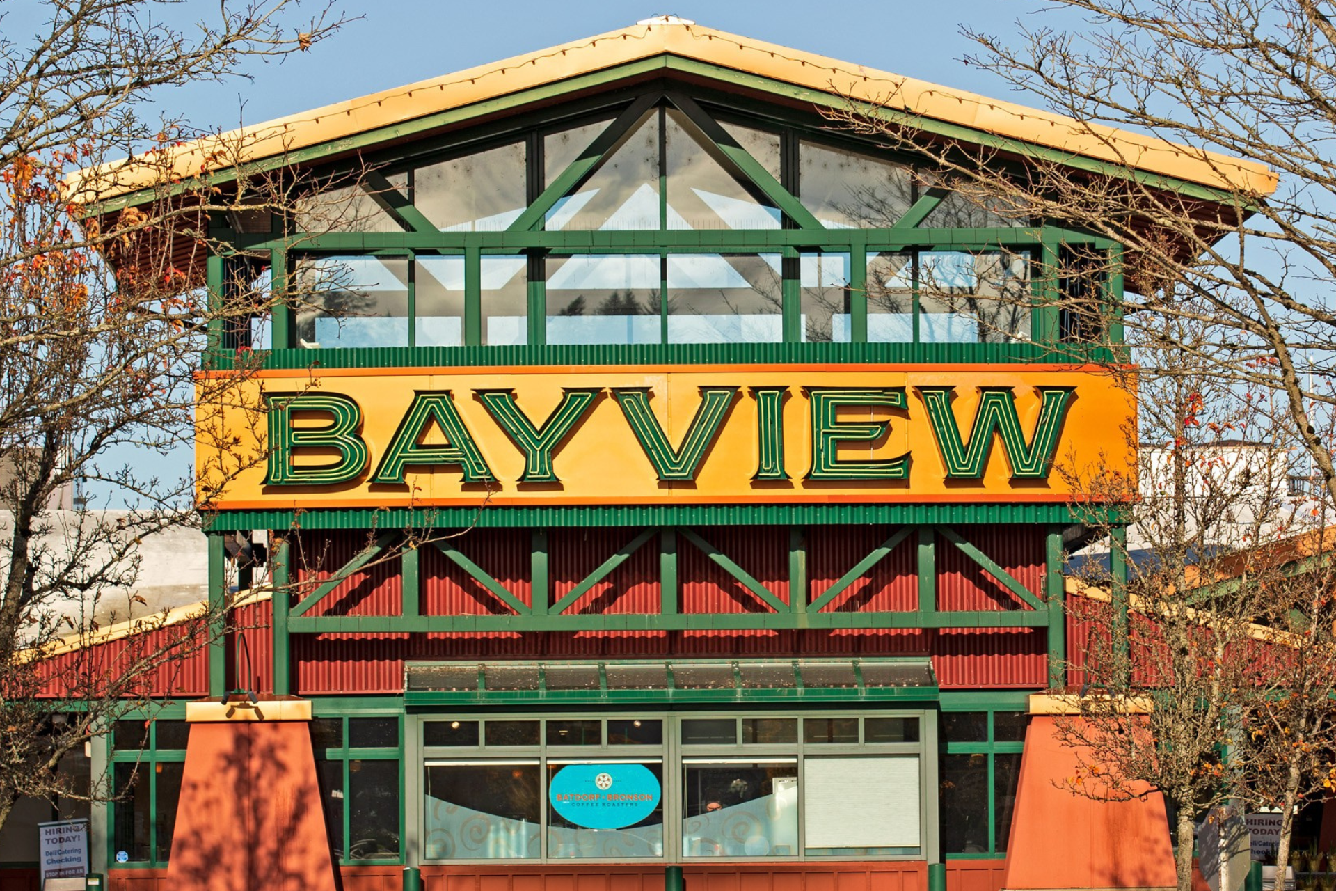 The image shows a building with a green and orange color scheme, and a large sign that reads 'BAYVIEW' in green letters on an orange background. The building has large windows and is surrounded by leafless trees.