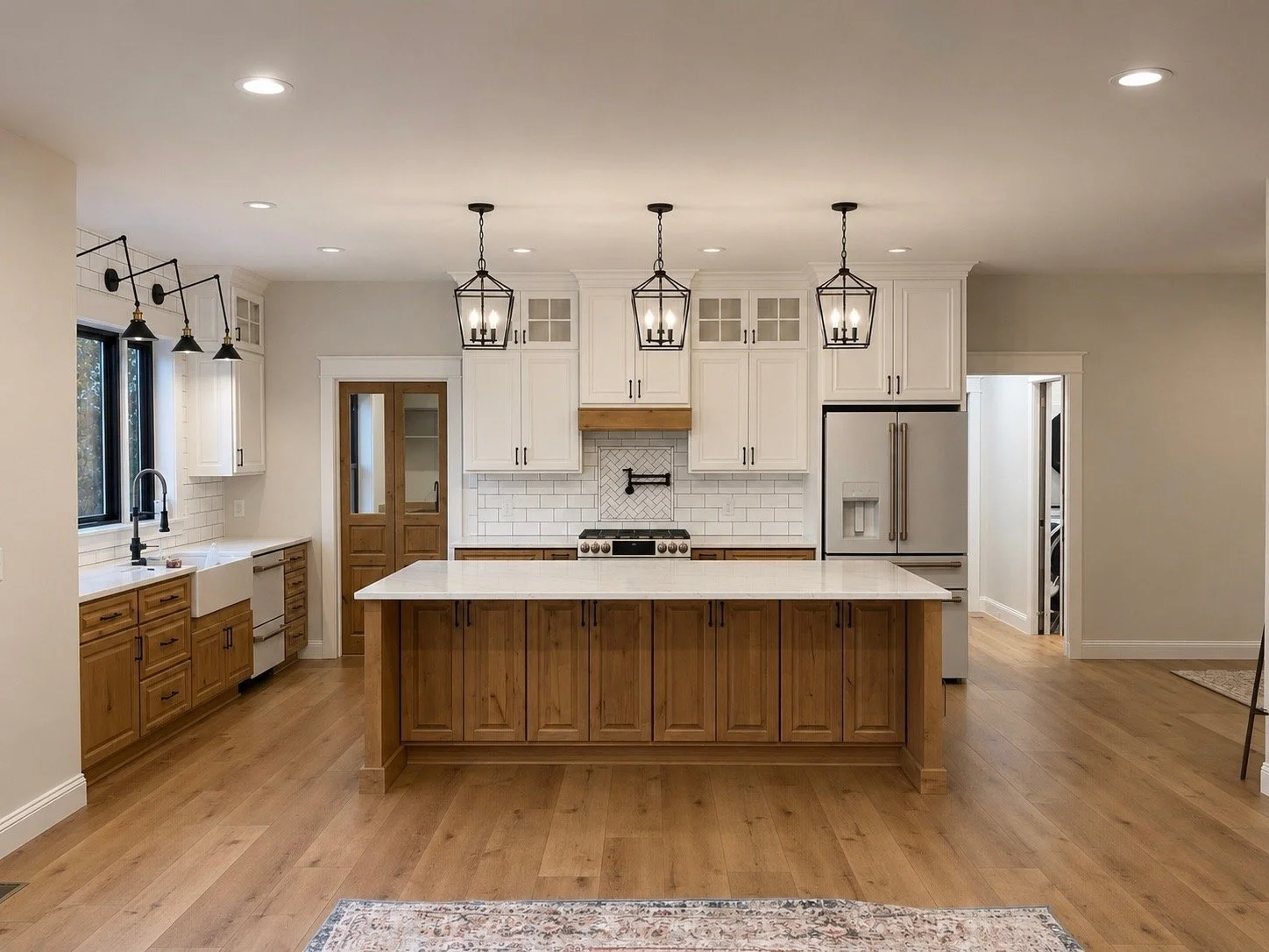 Modern kitchen with white cabinets, stainless steel refrigerator, wooden accents, island with white countertop, pendant and track lighting, farmhouse sink, and hardwood flooring.