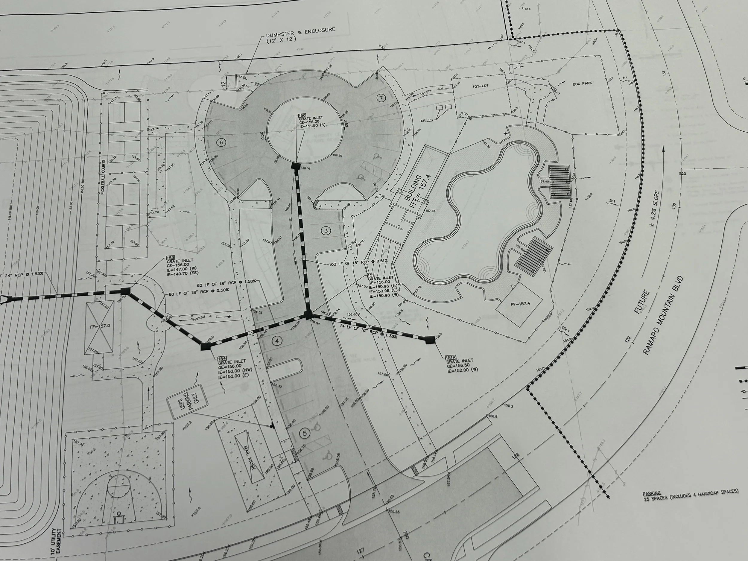 Architectural blueprint of a park or recreational area including a pond, playground, parking lot, trails, and various designated zones.