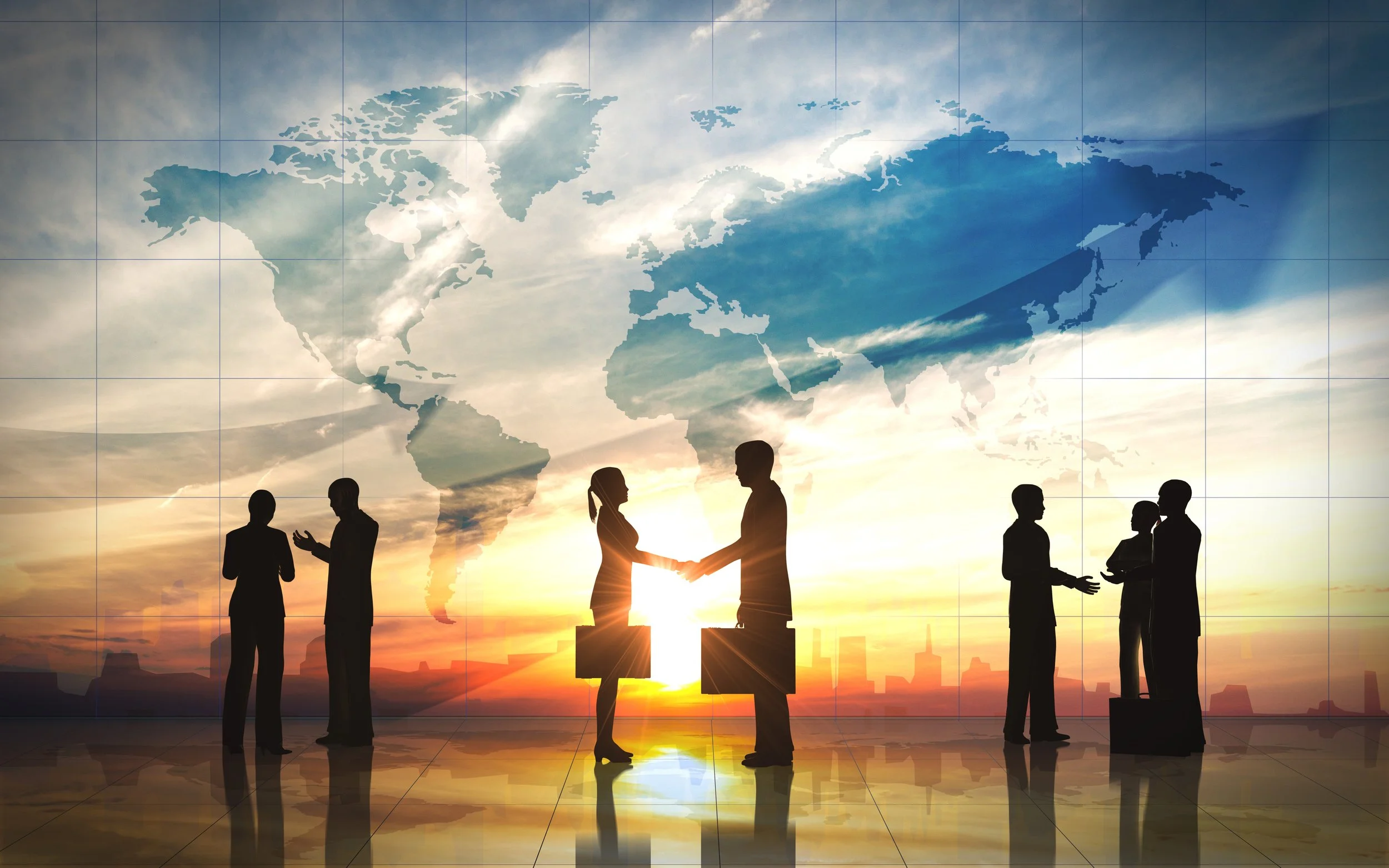 Silhouettes of businesspeople shaking hands and talking, with a large world map projected on a glass wall in the background, during sunset.