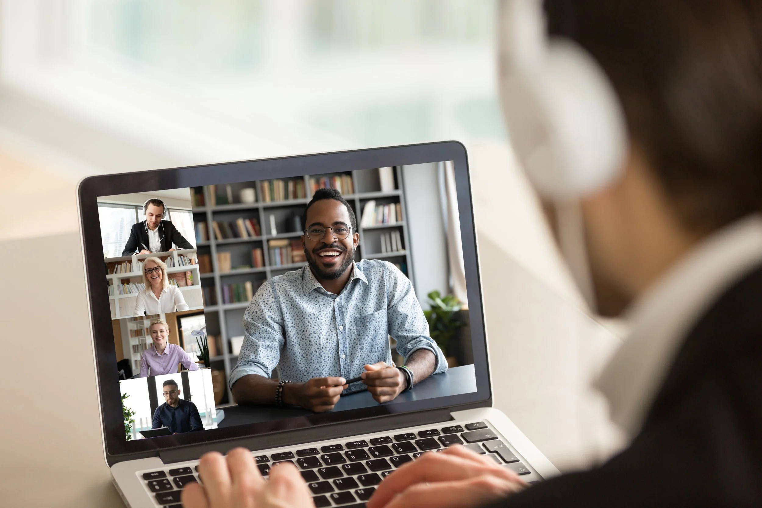 Video call on a laptop with five participants, including three men and two women, smiling and engaging in conversation.