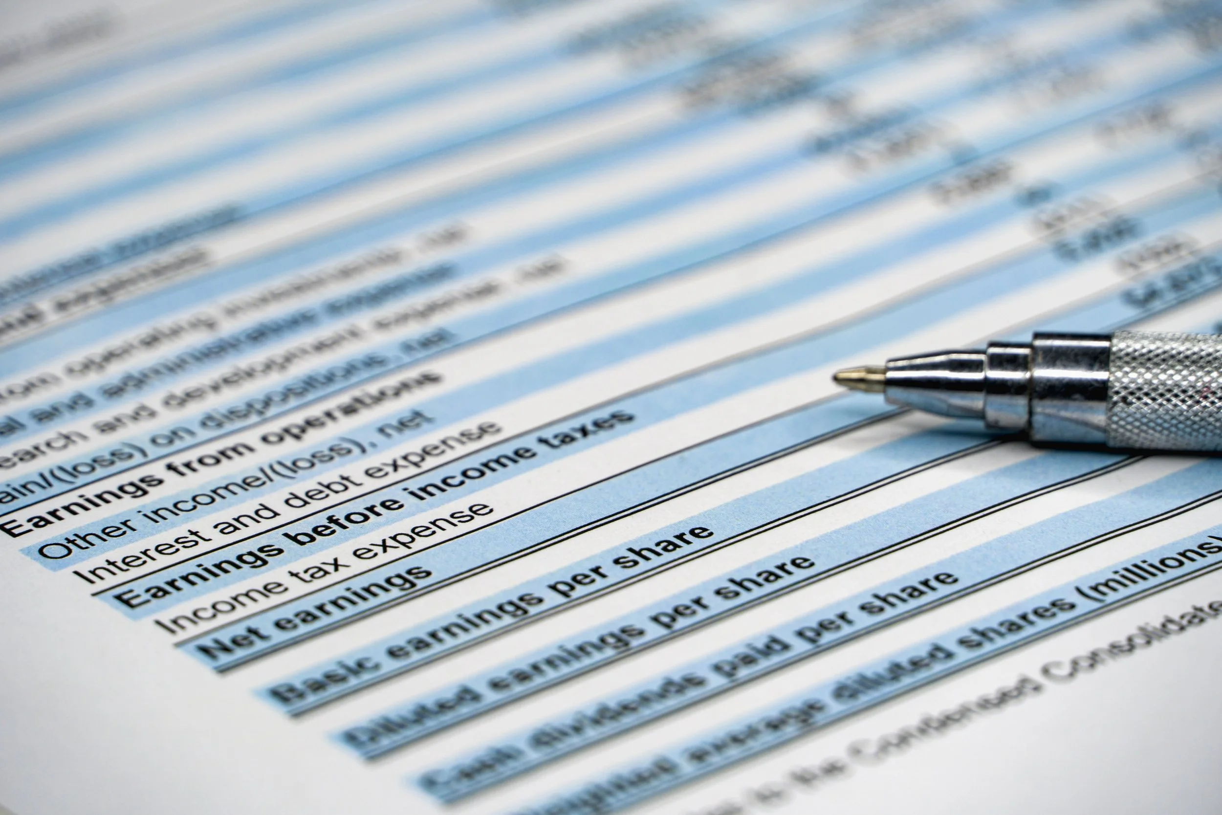 Close-up of a document related to taxes or financial filing, with black text on white paper and a metal pen resting on it.