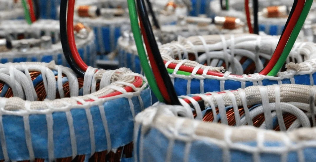 Close-up of multiple stator coils with copper wiring and American flag-colored wires, wrapped in blue insulation and white covering.