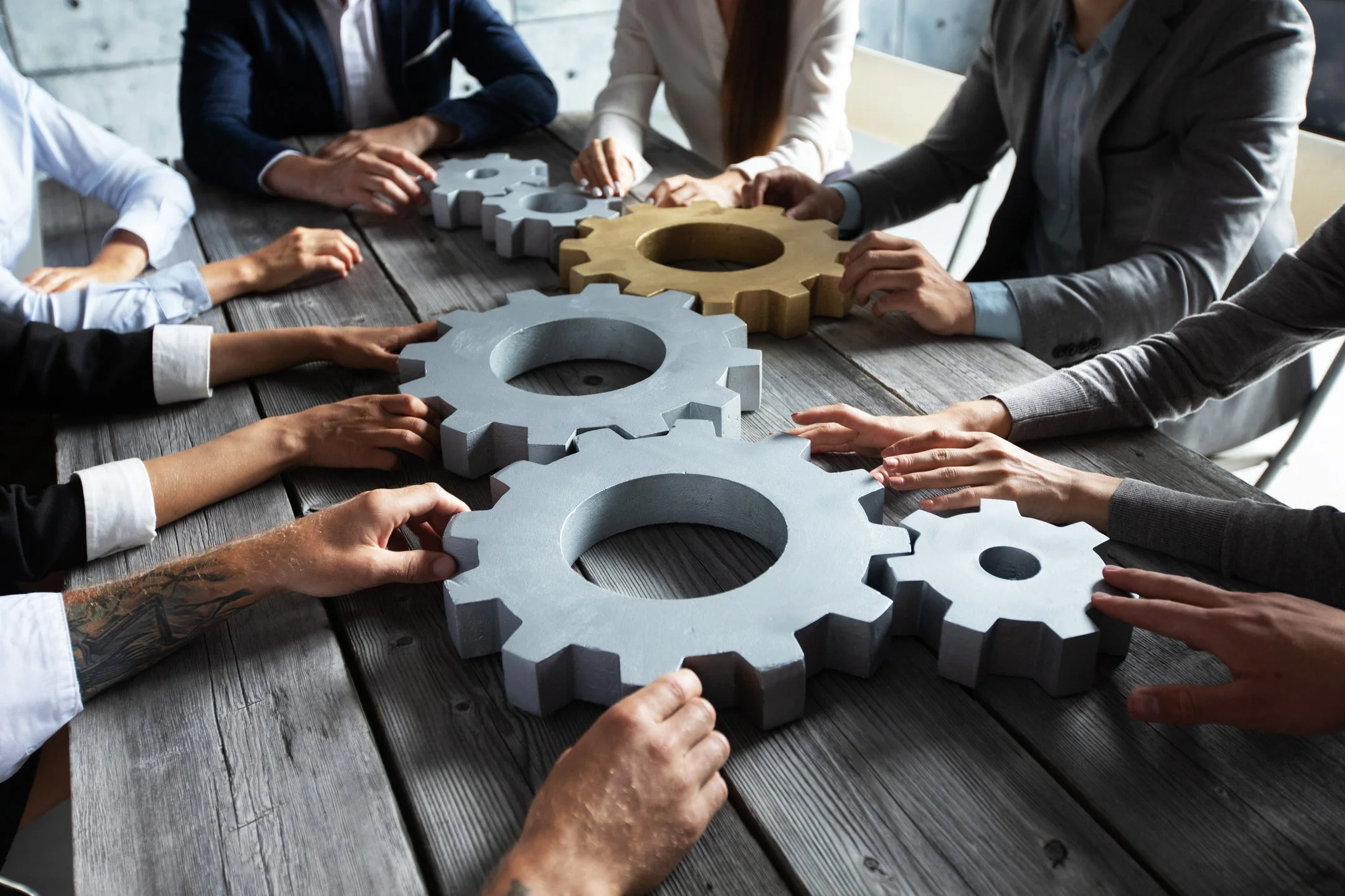 Group of people sitting around a wooden table, arranging metal and wooden gears.