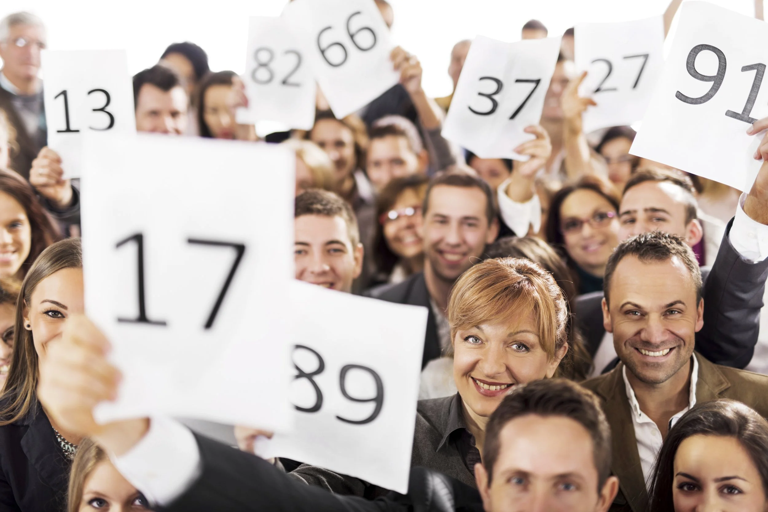 A large group of people smiling and holding up numbered posters in a crowded indoor setting.