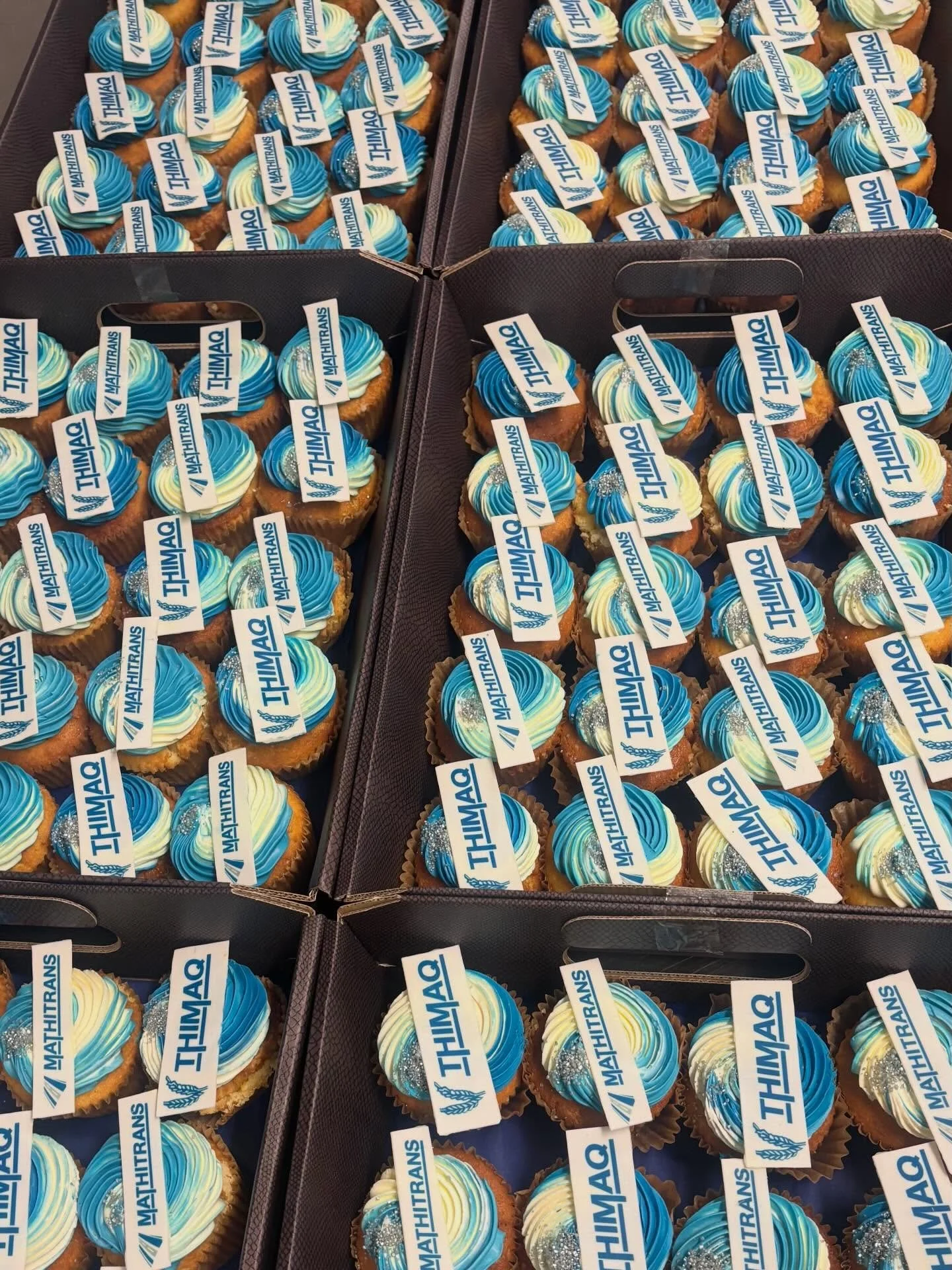 Tray of cupcakes decorated with blue and white swirled frosting, silver edible beads, and 'THINK' toppers featuring the MathITRANS logo.