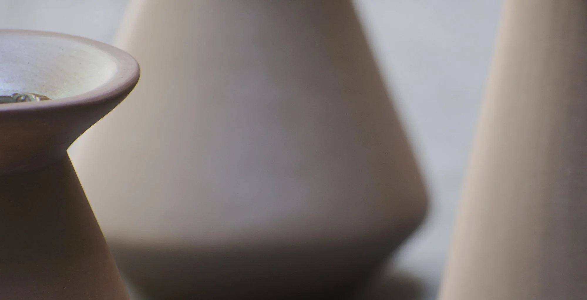 Close-up of a ceramic bowl with a light-colored interior and a dark exterior, positioned on a surface with shadows and soft lighting.