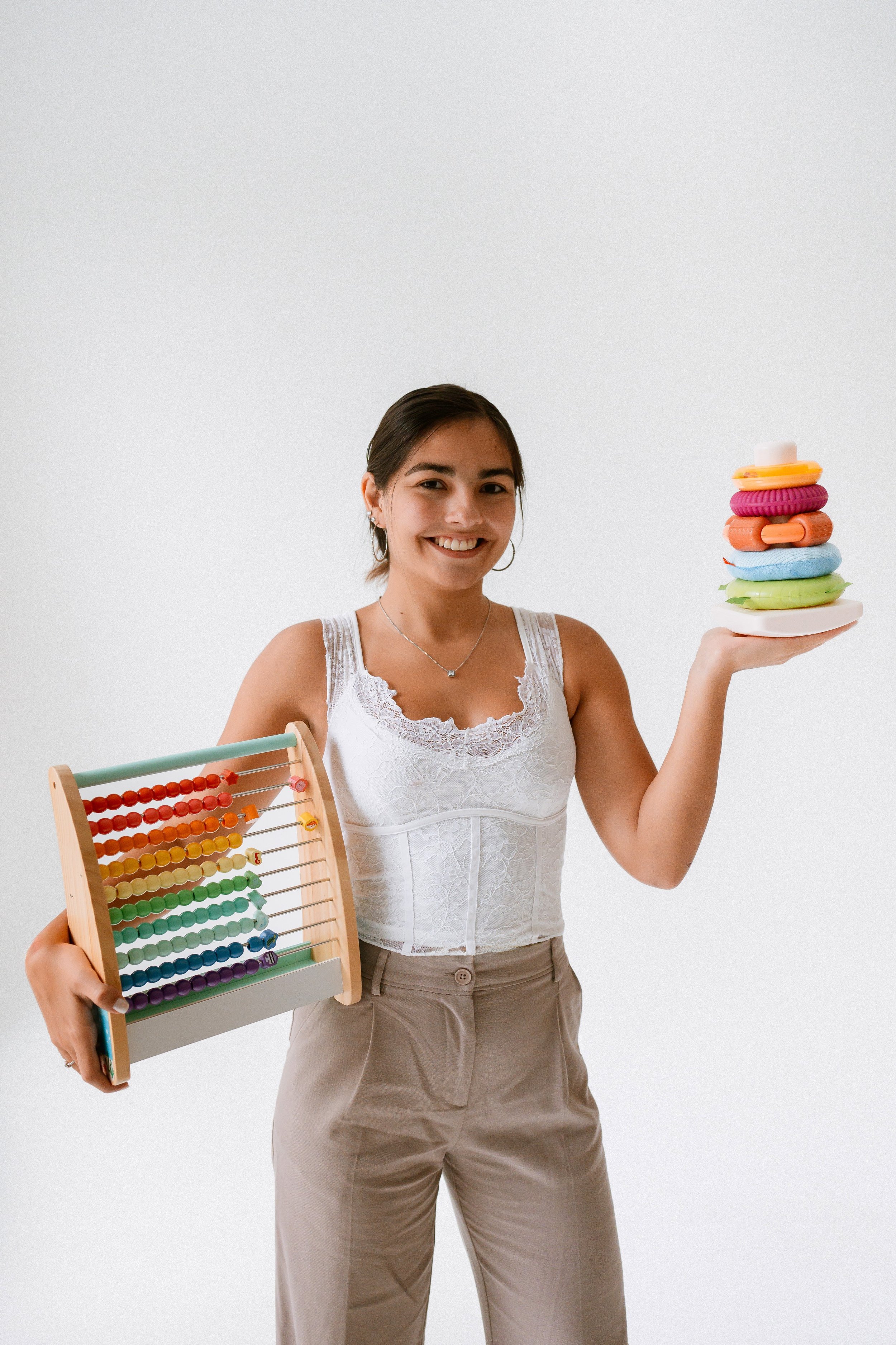 A woman smiling and holding a colorful abacus in one hand and a stack of colorful hair ties on a plate in the other.