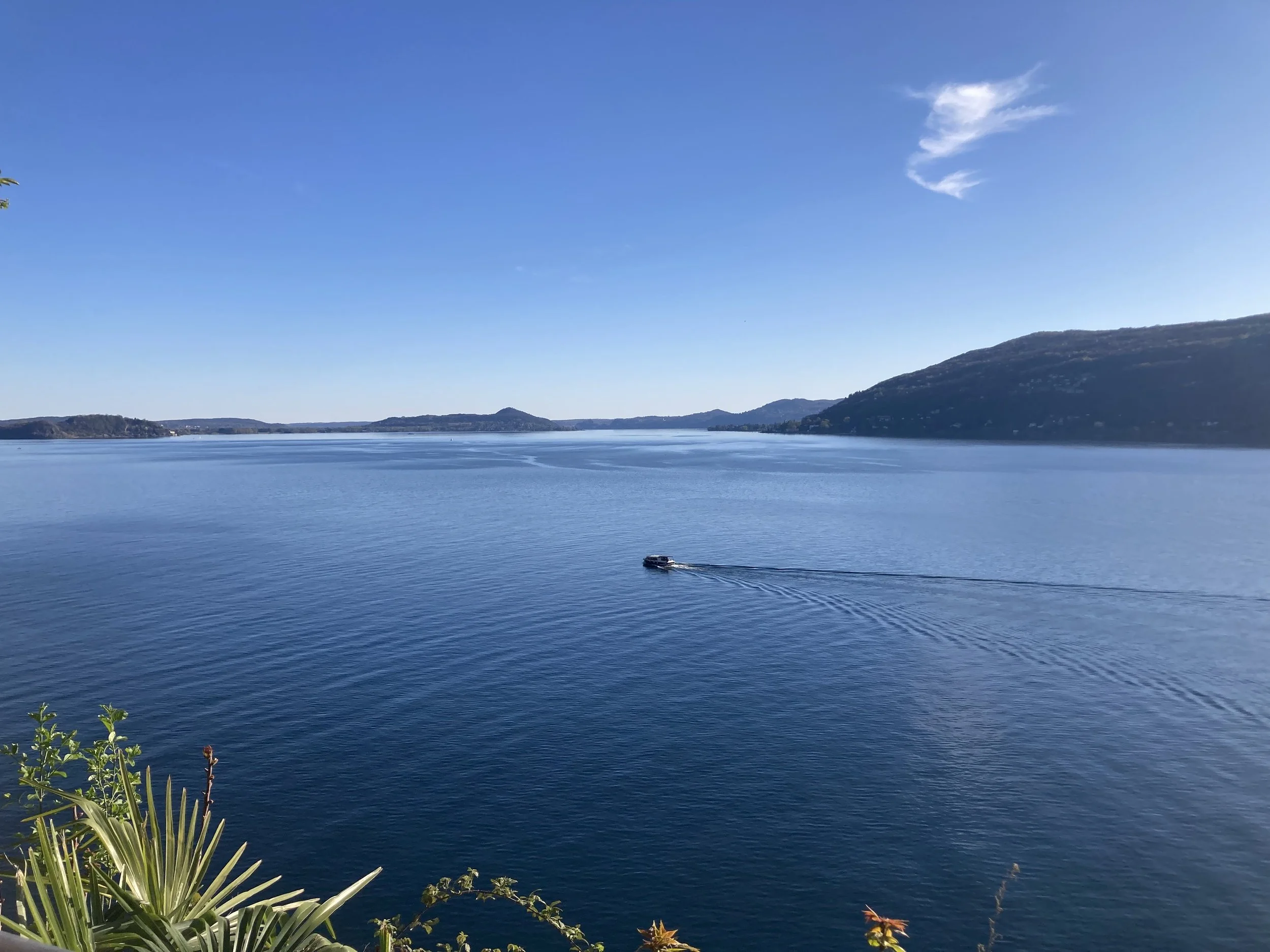 Blick über einen See mit Bergen im Hintergrund, blauer Himmel und eine kleine Boot auf dem Wasser
