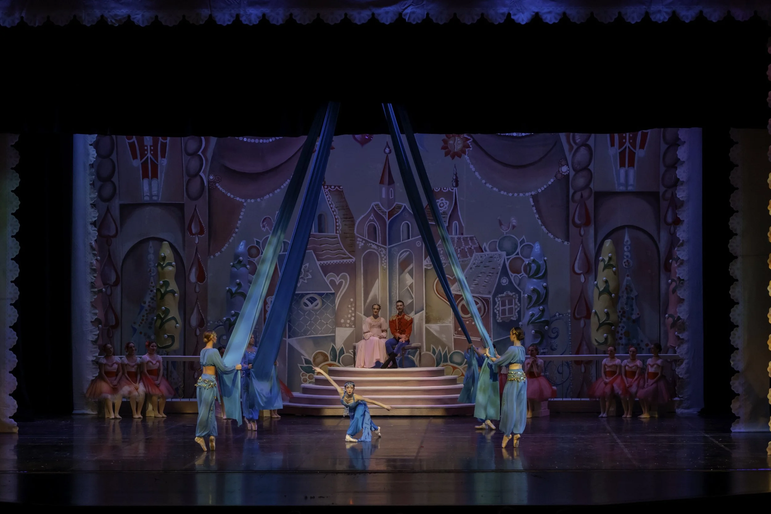 Ballet performance on stage with a colorful fantasy castle backdrop, dancers dressed in pastel costumes, in a theatrical production.