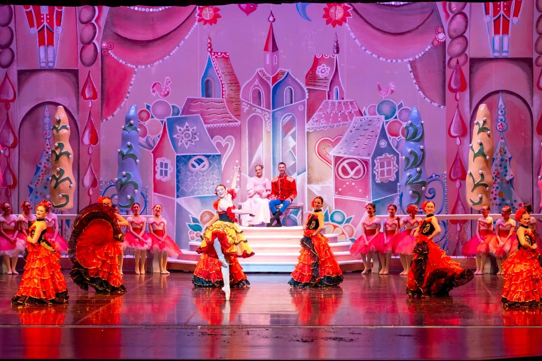 Ballet dancers in colorful costumes performing on stage with a fairy tale castle and whimsical backdrop.