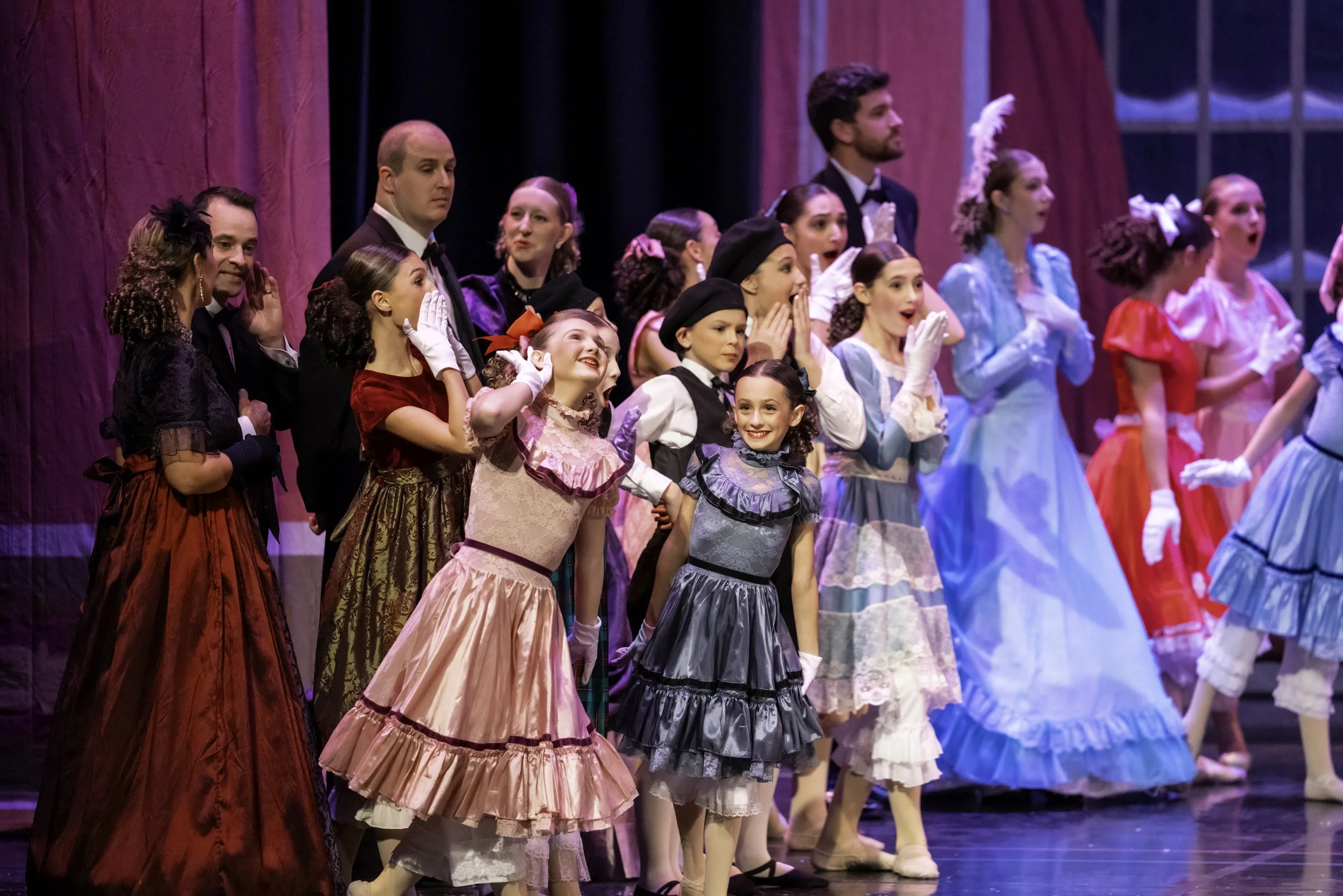 The cast of a theatrical production, dressed in elaborate period costumes, taking a bow on stage at the end of a performance.