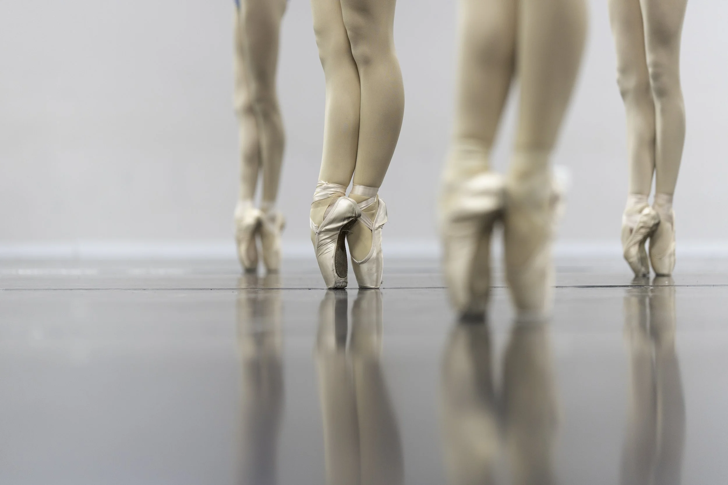 Close-up of ballet dancers' legs and feet in pointe shoes on a dance studio floor