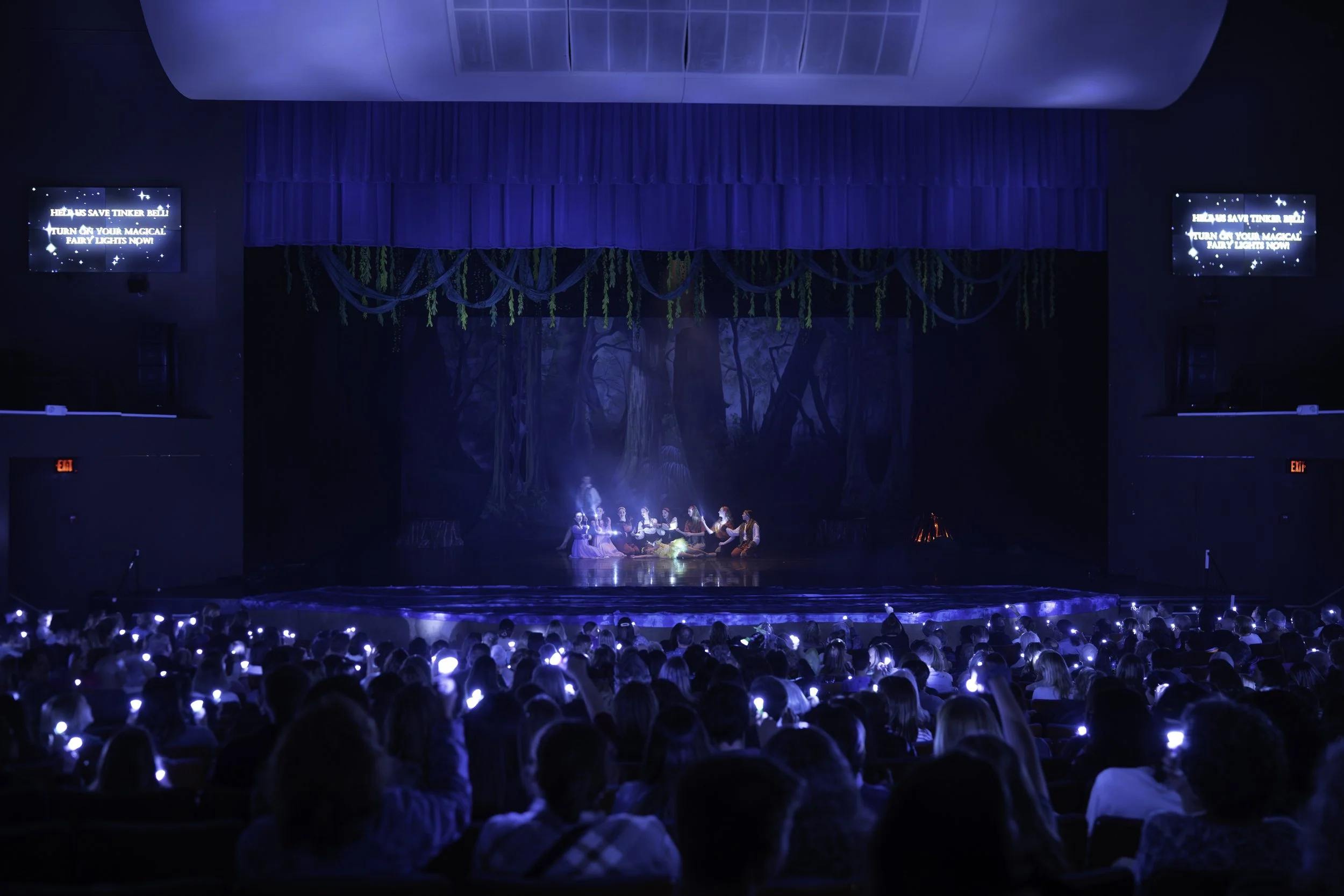 Theatre stage with a Disney's Frozen-themed backdrop, actors in costume, and an audience wearing glowing headbands.