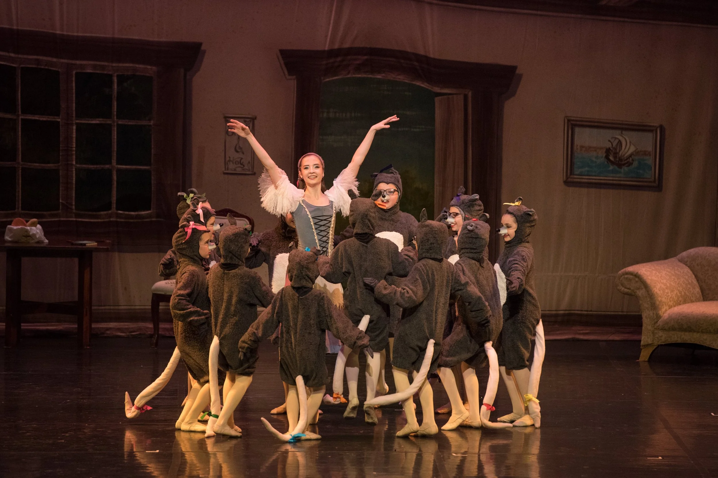 A woman in a costume performing on stage with children dressed as mice surrounding her.