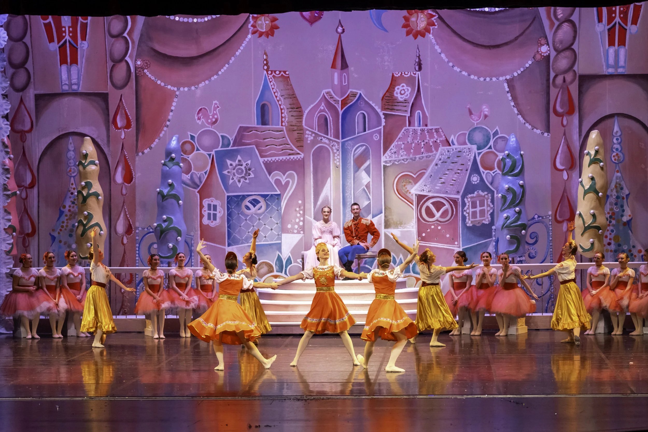 Ballet dancers performing on stage with colorful backdrop of a fantasy town.