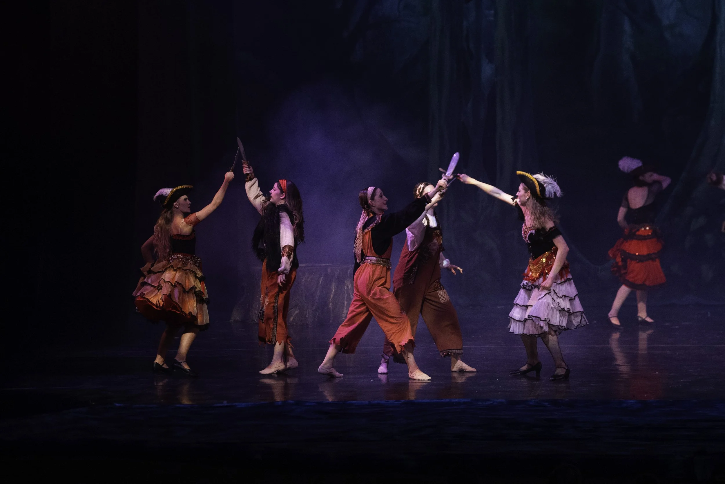 Performers dressed as pirates dance on stage, holding swords.